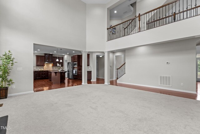 316 Hilliard Forest Dr, Cary, NC 27519 - unfurnished living room featuring ornate columns, a towering ceiling, dark carpet, stairs, and dark wood-style flooring