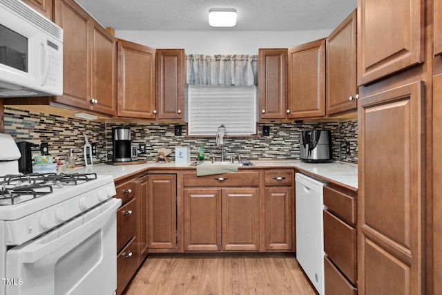 196 Red Wing Dr, Louisburg, NC 27549 - kitchen with white appliances, brown cabinetry, backsplash, light wood-style flooring, and a textured ceiling