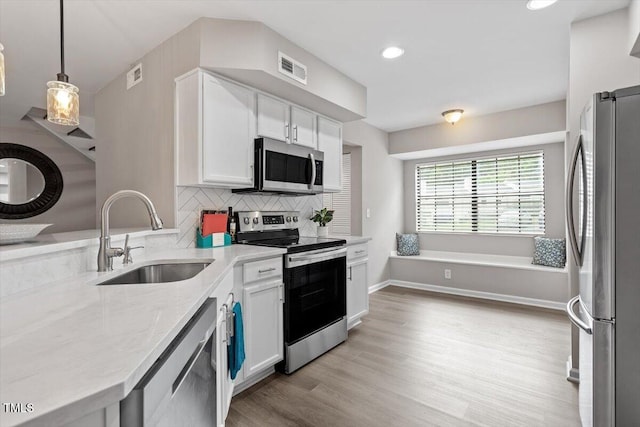 7771 Falcon Rest Cir, Raleigh, NC 27615 - kitchen with stainless steel appliances, white cabinetry, light wood-style flooring, tasteful backsplash, and decorative light fixtures