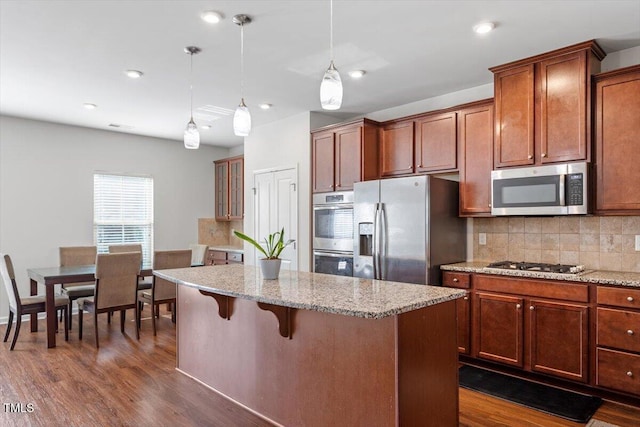 1035 Brownsmith Dr, Apex, NC 27502 - kitchen featuring appliances with stainless steel finishes, a kitchen island, decorative backsplash, light stone countertops, and dark wood finished floors