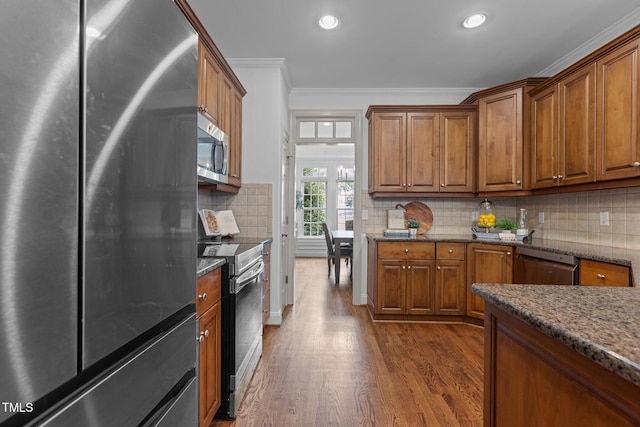 6104 Spicewood Dr, Fuquay Varina, NC 27526 - kitchen with appliances with stainless steel finishes, ornamental molding, brown cabinets, dark wood finished floors, and dark stone counters