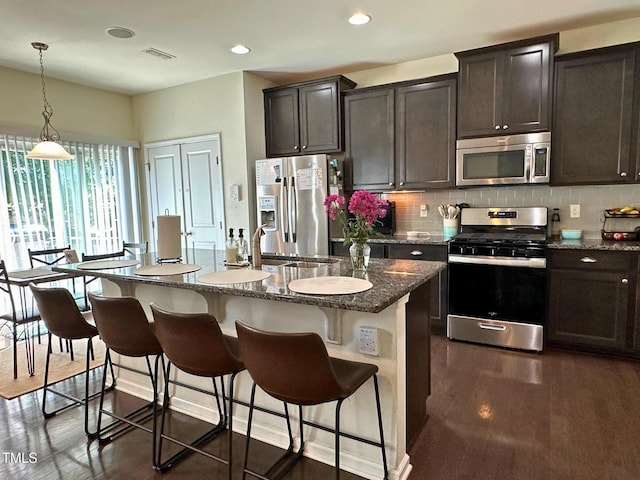 505 Poplar St, Durham, NC 27703 - kitchen with appliances with stainless steel finishes, dark wood finished floors, dark stone counters, decorative backsplash, and a kitchen breakfast bar