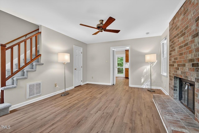 10 Tarawa Ter, Durham, NC 27705 - unfurnished living room featuring ceiling fan, wood finished floors, a brick fireplace, and stairs