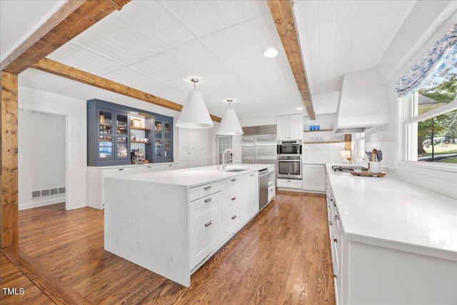 8909 Hunting Trl, Raleigh, NC 27613 - kitchen featuring appliances with stainless steel finishes, beamed ceiling, light countertops, wood finished floors, and glass insert cabinets