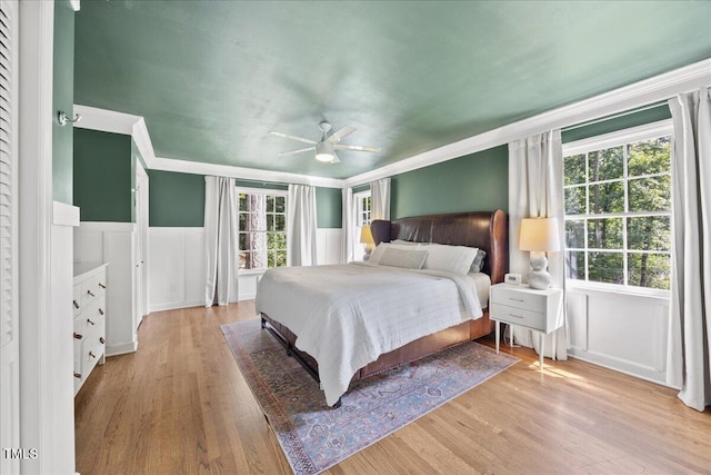 8909 Hunting Trl, Raleigh, NC 27613 - bedroom featuring wainscoting, light wood-style flooring, ornamental molding, a decorative wall, and ceiling fan