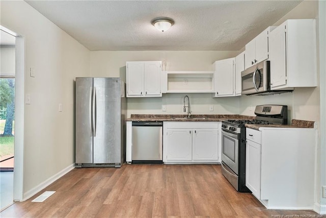 2619 Dumfries Dr, Fayetteville, NC 28306 - kitchen with stainless steel appliances, dark countertops, open shelves, light wood-style flooring, and a textured ceiling