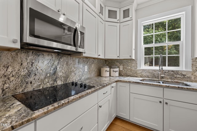1802 Abby Knoll Dr, Apex, NC 27502 - kitchen featuring stainless steel microwave, black electric stovetop, white cabinetry, light stone countertops, and decorative backsplash