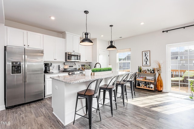 235 Misty Pike Dr, Raleigh, NC 27603 - kitchen featuring appliances with stainless steel finishes, wood finished floors, an island with sink, white cabinetry, and light stone countertops
