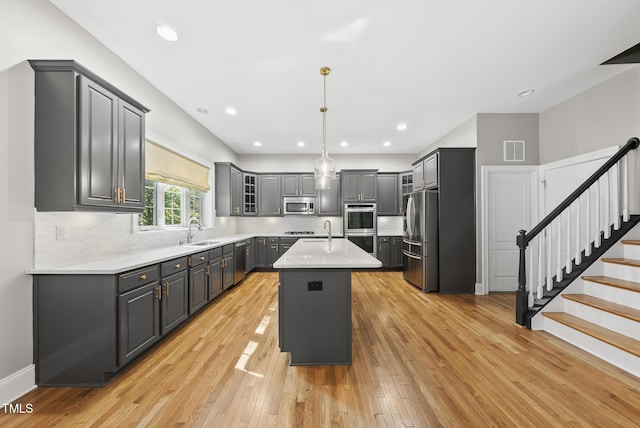 7112 Hasentree Way, Wake Forest, NC 27587 - kitchen with stainless steel appliances, an island with sink, gray cabinets, light countertops, and light wood finished floors