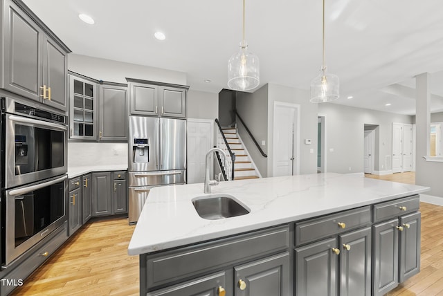 7112 Hasentree Way, Wake Forest, NC 27587 - kitchen with appliances with stainless steel finishes, gray cabinets, a center island with sink, light wood-style floors, and glass insert cabinets