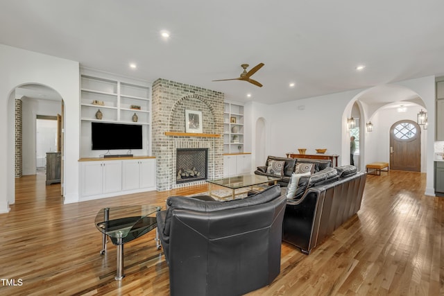 2203 Meadowcreek Dr, Durham, NC 27705 - living area featuring arched walkways, a ceiling fan, light wood-style floors, a fireplace, and built in shelves