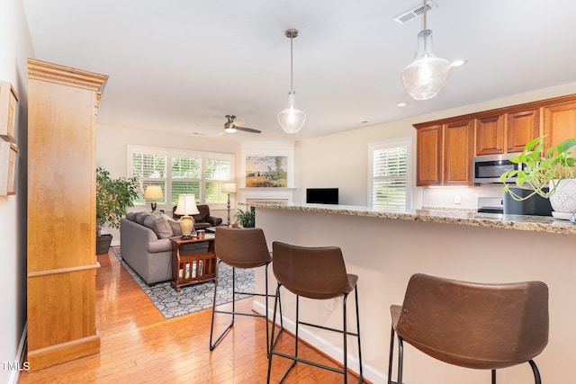 5030 Homeplace Dr, Apex, NC 27539 - kitchen with stainless steel microwave, light wood-style flooring, a kitchen bar, brown cabinetry, and decorative light fixtures