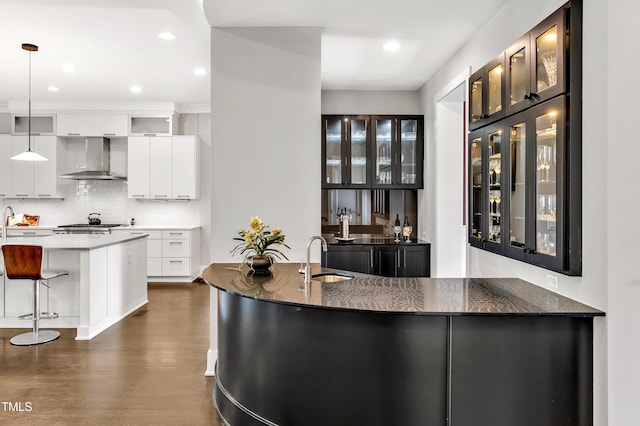 5040 Shakori Trl, Durham, NC 27707 - kitchen featuring wall chimney exhaust hood, a breakfast bar area, backsplash, dark wood finished floors, and glass insert cabinets
