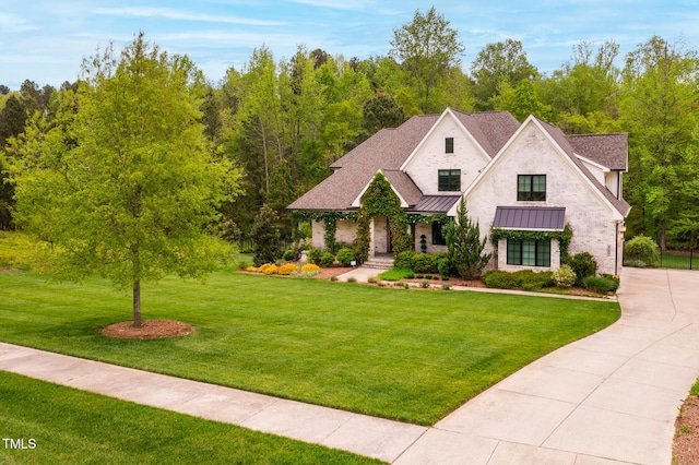 5040 Shakori Trl, Durham, NC 27707 - french country style house featuring a standing seam roof, driveway, a front yard, a shingled roof, and a view of trees