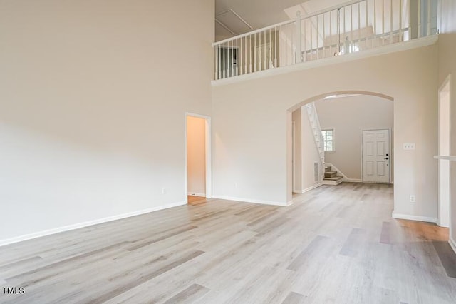 5933 Big Nance Dr, Raleigh, NC 27616 - unfurnished living room featuring arched walkways, wood finished floors, a towering ceiling, and stairs