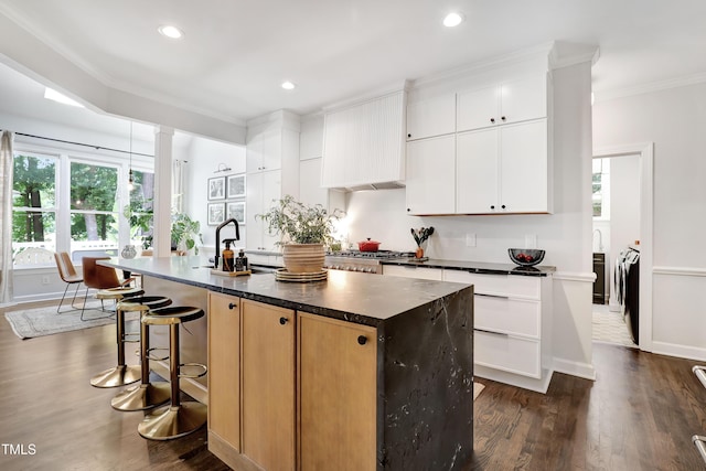 5004 Sunset Forest Cir, Holly Springs, NC 27540 - kitchen with crown molding, dark wood-style flooring, a kitchen island with sink, a breakfast bar area, and dark countertops