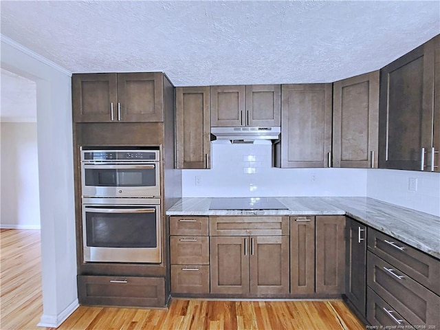 7246 Faircloth Bridge Rd, Stedman, NC 28391 - kitchen with black electric stovetop, stainless steel double oven, under cabinet range hood, light wood-type flooring, and crown molding