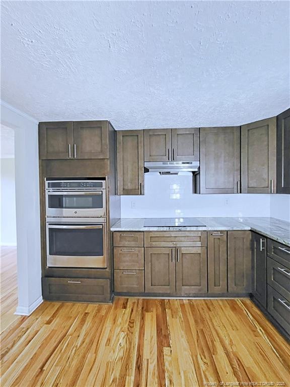 7246 Faircloth Bridge Rd, Stedman, NC 28391 - kitchen featuring under cabinet range hood, light wood-style floors, stainless steel double oven, black electric stovetop, and a textured ceiling