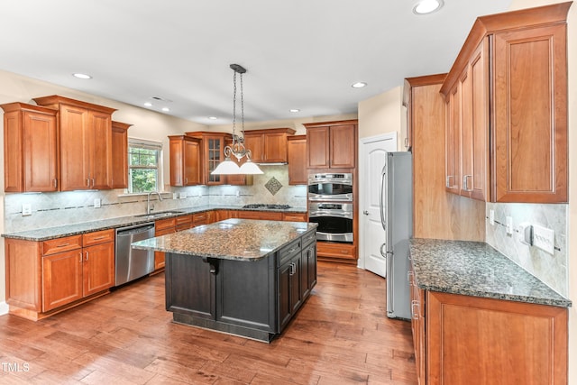 428 Holsten Bank Way, Cary, NC 27519 - kitchen with appliances with stainless steel finishes, a kitchen island, brown cabinetry, dark stone counters, and recessed lighting