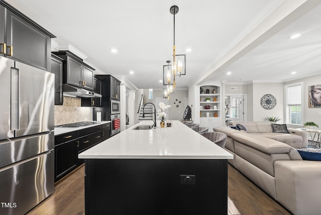 7741 Wilderness Rd, Raleigh, NC 27613 - kitchen featuring appliances with stainless steel finishes, open floor plan, dark cabinetry, decorative backsplash, and an island with sink