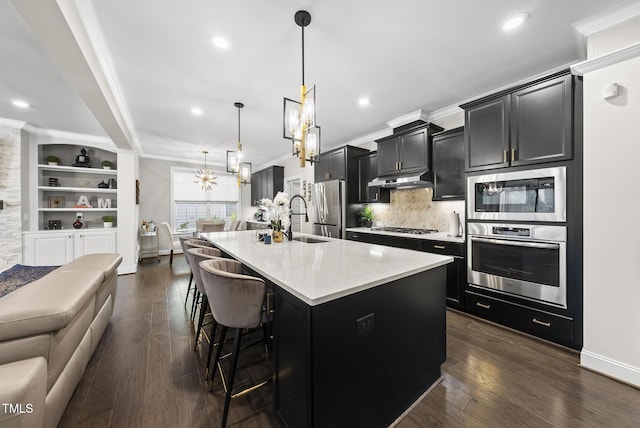 7741 Wilderness Rd, Raleigh, NC 27613 - kitchen with appliances with stainless steel finishes, dark cabinets, crown molding, a kitchen island with sink, and decorative backsplash