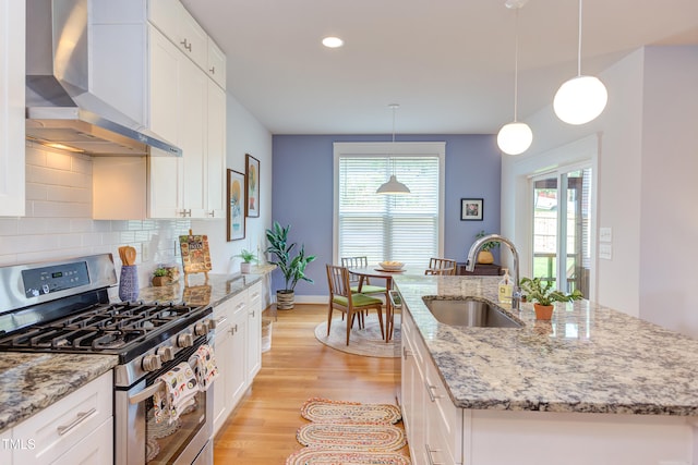 119 W Piedmont Ave, Durham, NC 27707 - kitchen featuring wall chimney exhaust hood, stainless steel range with gas stovetop, a kitchen island with sink, tasteful backsplash, and light wood finished floors