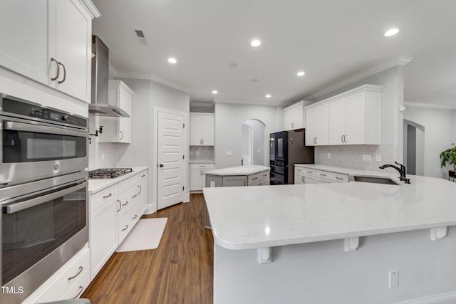 425 Cahors Trl, Holly Springs, NC 27540 - kitchen featuring appliances with stainless steel finishes, wall chimney exhaust hood, crown molding, tasteful backsplash, and a peninsula