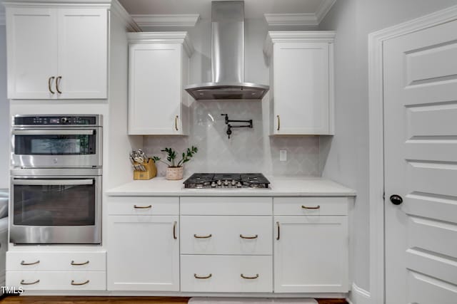 425 Cahors Trl, Holly Springs, NC 27540 - kitchen with wall chimney exhaust hood, stainless steel appliances, light countertops, white cabinetry, and ornamental molding