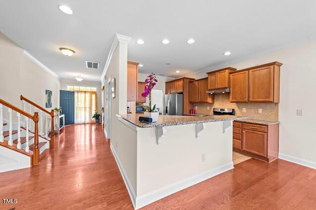 4007 Strendal Dr, Cary, NC 27519 - kitchen featuring stainless steel refrigerator with ice dispenser, crown molding, under cabinet range hood, brown cabinets, and light wood-type flooring