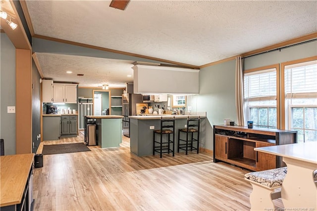 1360 Rays Bridge Rd, Whispering Pines, NC 28327 - kitchen featuring crown molding, a breakfast bar area, a textured ceiling, a peninsula, and light wood-style floors
