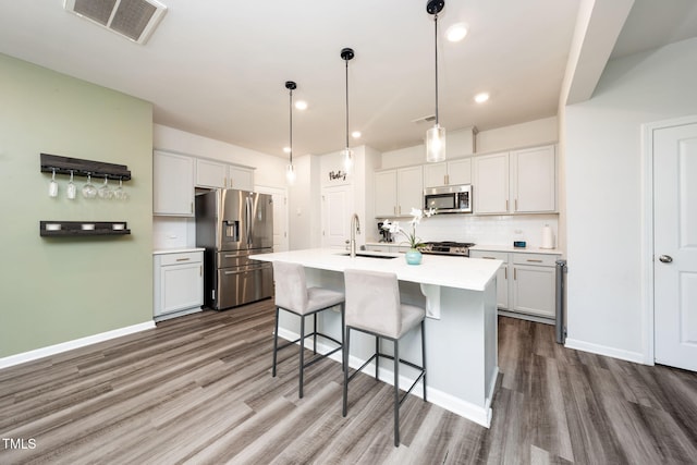 1143 Sweet Cream Ct, Durham, NC 27703 - kitchen featuring appliances with stainless steel finishes, wood finished floors, a kitchen bar, tasteful backsplash, and light countertops