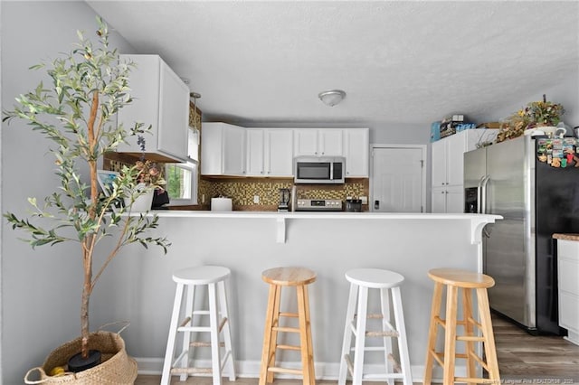 4450 Chesterbrook Dr, Fayetteville, NC 28314 - kitchen with stainless steel appliances, a peninsula, white cabinetry, wood finished floors, and a breakfast bar area