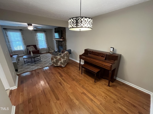 106 Carmel Woods Ct, Wake Forest, NC 27587 - sitting room featuring wood finished floors, a textured ceiling, a fireplace with raised hearth, and a ceiling fan