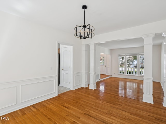 104 Pellinore Ct, Cary, NC 27513 - unfurnished dining area with decorative columns, light wood finished floors, a chandelier, a wainscoted wall, and a decorative wall