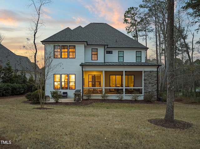 2105 Gardenbrook Dr, Raleigh, NC 27606 - back of property at dusk with a standing seam roof, a porch, a shingled roof, a lawn, and a metal roof