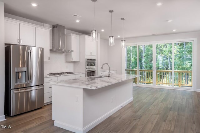 4703 Mint Leaf Ln, Raleigh, NC 27612 - kitchen featuring appliances with stainless steel finishes, wall chimney range hood, wood finished floors, white cabinets, and an island with sink