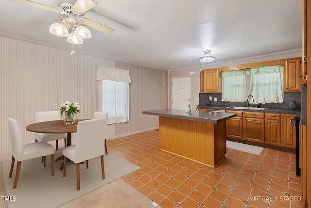 3702 Danube Ln, Durham, NC 27704 - kitchen with ornamental molding, a kitchen island, dark countertops, a ceiling fan, and stainless steel dishwasher