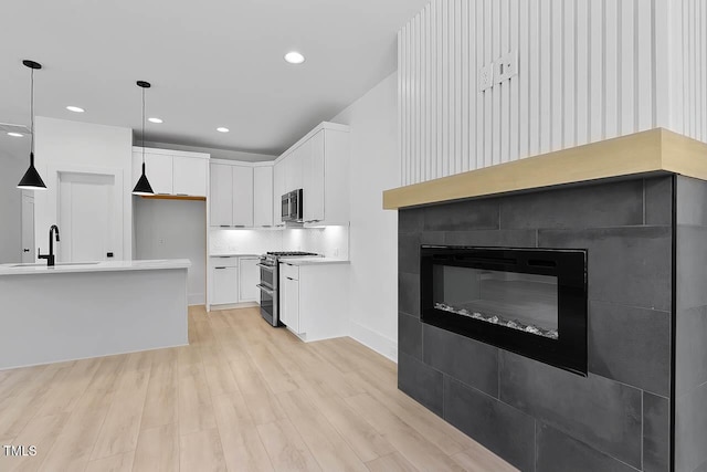 140 E End Ave, Durham, NC 27703 - kitchen with stainless steel appliances, light wood-style flooring, white cabinetry, a glass covered fireplace, and recessed lighting