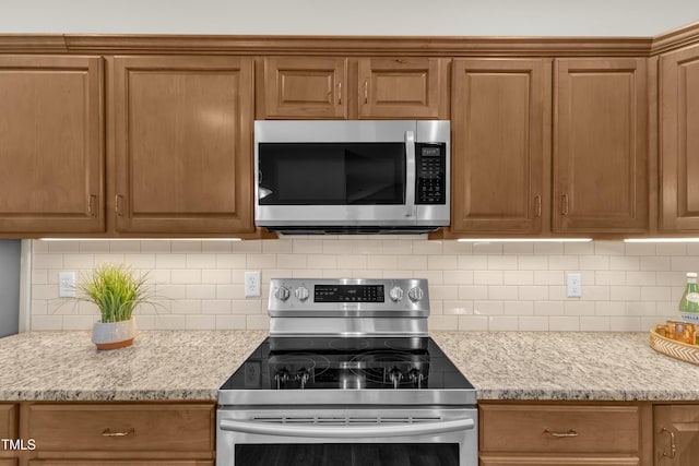 4710 Ludwell Branch Ct, Raleigh, NC 27612 - kitchen featuring appliances with stainless steel finishes, backsplash, brown cabinetry, and light stone countertops