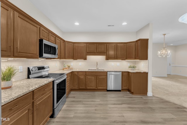 4710 Ludwell Branch Ct, Raleigh, NC 27612 - kitchen featuring appliances with stainless steel finishes, a chandelier, decorative backsplash, light stone countertops, and light wood-style floors