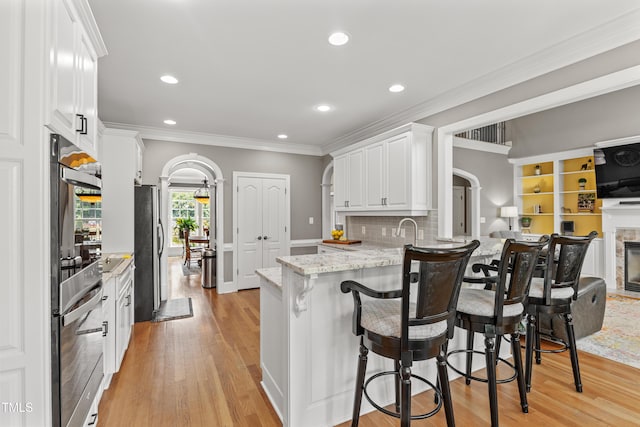 2512 Stewart St, Fuquay Varina, NC 27526 - kitchen with arched walkways, light wood-style flooring, a peninsula, white cabinetry, and ornamental molding