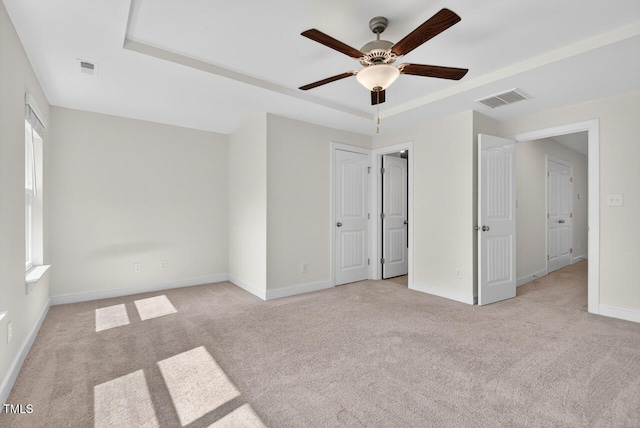 305 Lionel St, Durham, NC 27705 - unfurnished bedroom with carpet flooring, a tray ceiling, multiple windows, and a ceiling fan