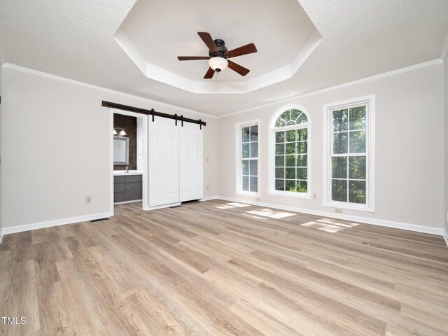 129 Nottingham Ct, Youngsville, NC 27596 - unfurnished bedroom featuring a raised ceiling, light wood-style flooring, a barn door, ensuite bath, and crown molding