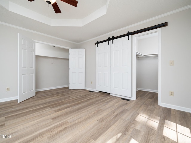 129 Nottingham Ct, Youngsville, NC 27596 - unfurnished bedroom with a barn door, a raised ceiling, light wood finished floors, a spacious closet, and ornamental molding