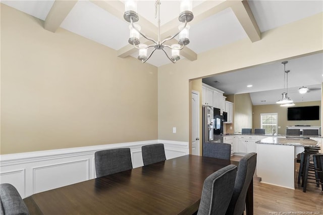 1657 Stackhouse Dr, Fayetteville, NC 28314 - dining space featuring a chandelier, beamed ceiling, a wainscoted wall, light wood-style floors, and a decorative wall