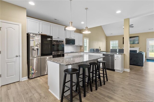 1657 Stackhouse Dr, Fayetteville, NC 28314 - kitchen with black appliances, light wood-style floors, white cabinets, a center island, and vaulted ceiling