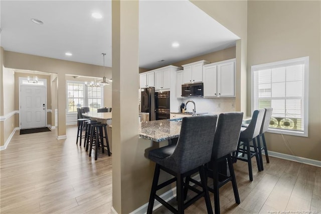 1657 Stackhouse Dr, Fayetteville, NC 28314 - kitchen with stainless steel appliances, a chandelier, a kitchen bar, light wood-type flooring, and white cabinets