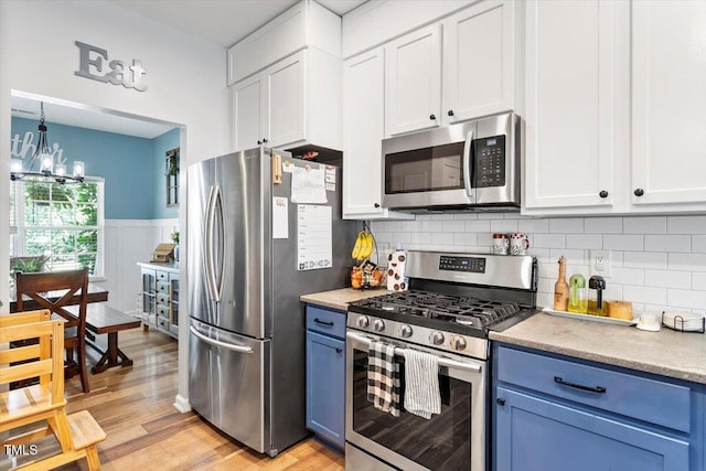 109 Covenant Rock Ln, Holly Springs, NC 27540 - kitchen featuring appliances with stainless steel finishes, blue cabinetry, a chandelier, light wood finished floors, and wainscoting