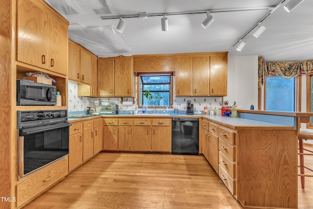 128 Chris Ct, Garner, NC 27529 - kitchen featuring black appliances, a peninsula, track lighting, light wood-type flooring, and a breakfast bar