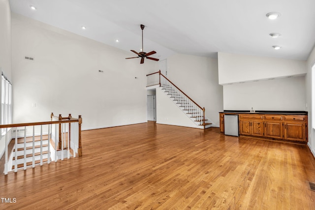 1820 Hunting Ridge Rd, Raleigh, NC 27615 - unfurnished living room with a ceiling fan, light wood-type flooring, stairs, high vaulted ceiling, and bar area